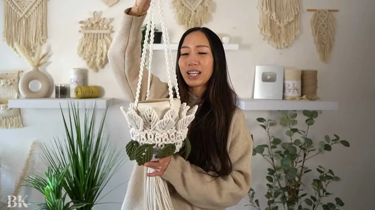 Holding a completed macrame plant hanger to show full height from ring to basket