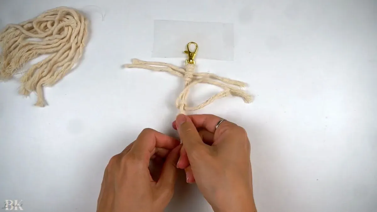 Hands demonstrating the double half hitch knotting technique for a macrame feather