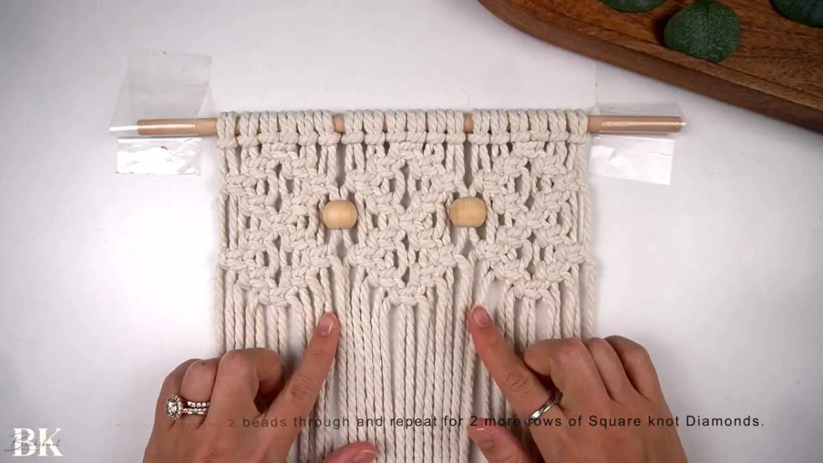Macrame wall hanging with multiple rows of diamonds and wooden beads in progress